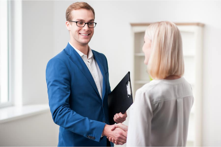 a man in a suit with a clipboard shaking hands with a woman
