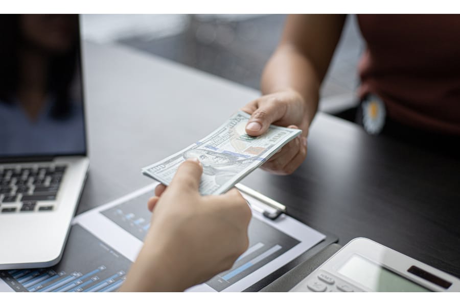 two people exchanging cash in hand over a desk