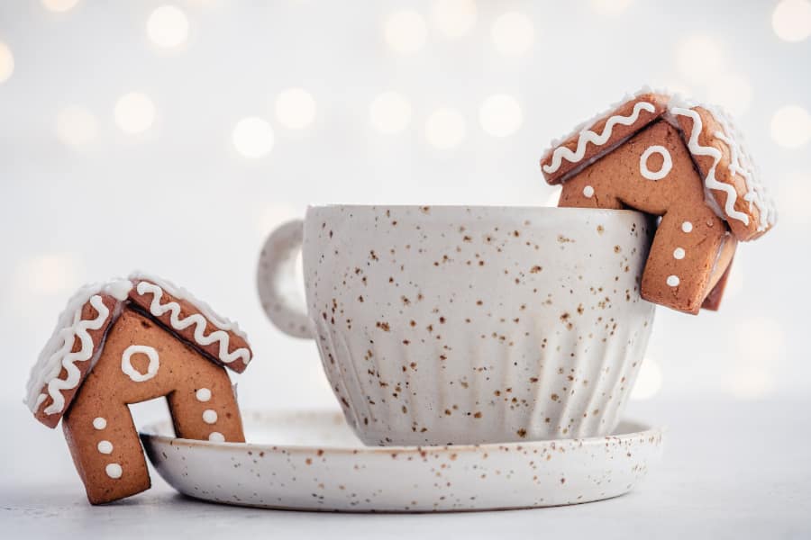 two mini gingerbread houses hanging with a cup