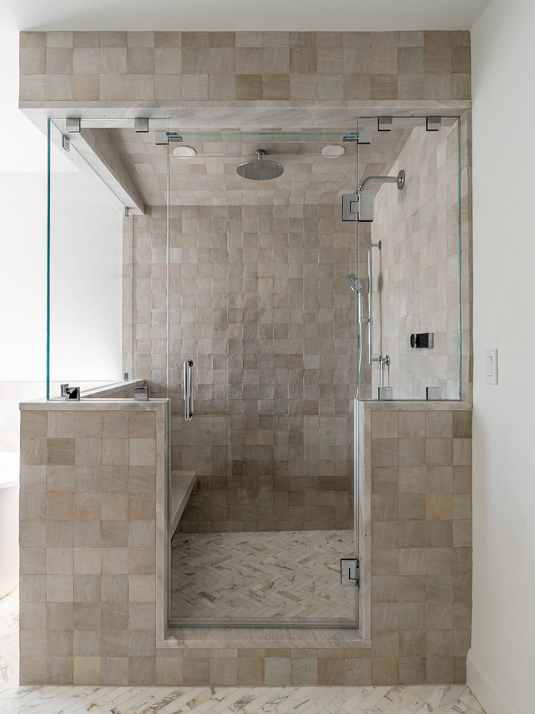 Frameless glass shower with transom and bench seat in a natural stone bathroom