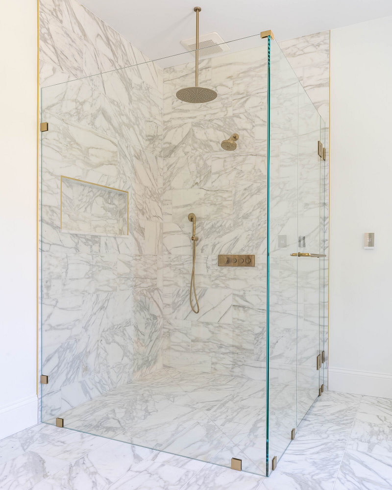 Ultra-clear low-iron frameless glass shower enclosure with brushed brass hardware and marble tile