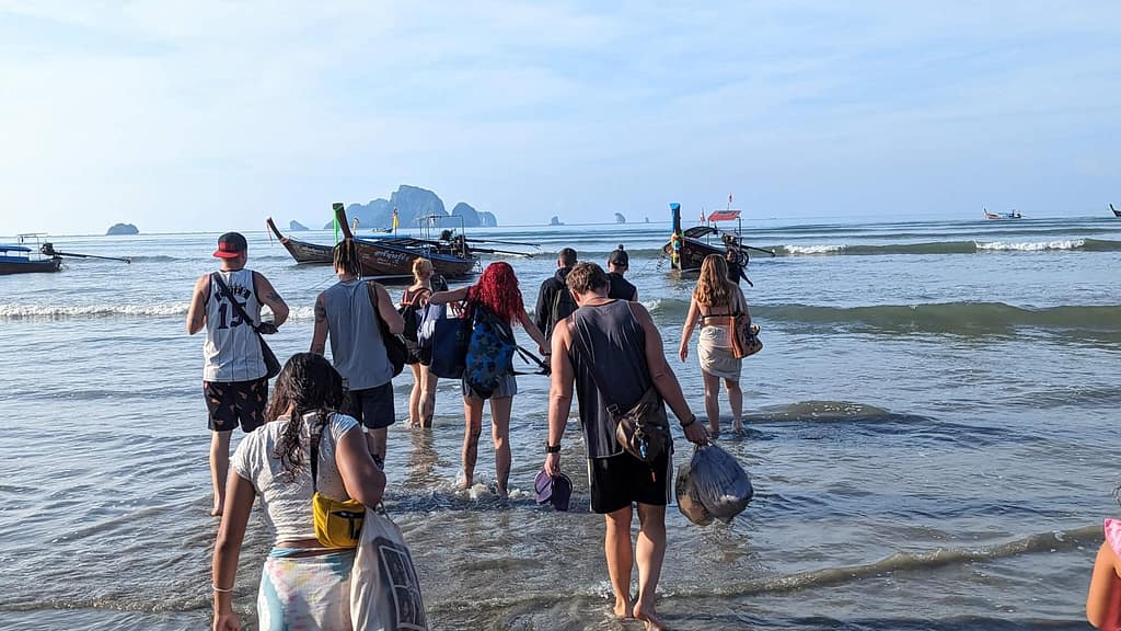 grupo de personas vadeando el agua hacia una barca de cola larga en krabi