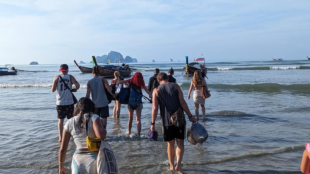 groups of people wading through the water at aonang beach to a longtail boat