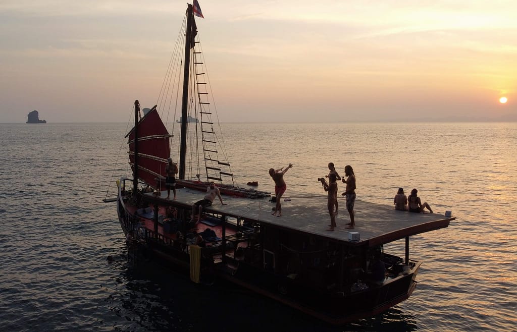 un hombre a punto de saltar de krabi puesta de sol crucero pirata barco cubierta superior, mientras que la gente mira y otra ver la salida del sol en el fondo