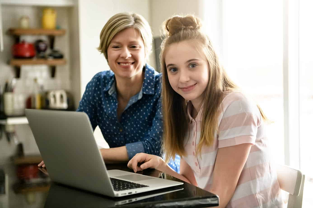 A happy mother and daughter setting up the Canopy app on their laptop in their kitchen