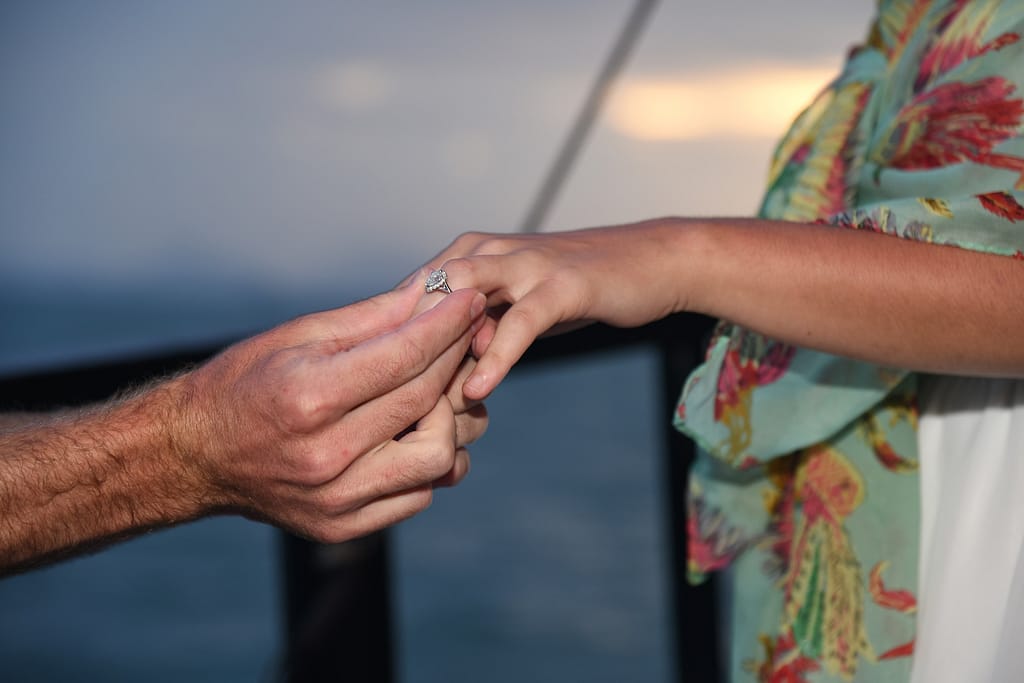 colocando un anillo de boda en un dedo con la puesta de sol de fondo