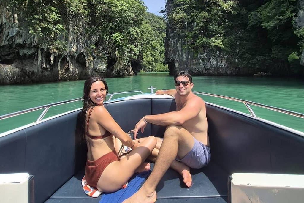 a couple at the front of a speedboat with thailands turquiose waters and cliffs in the background