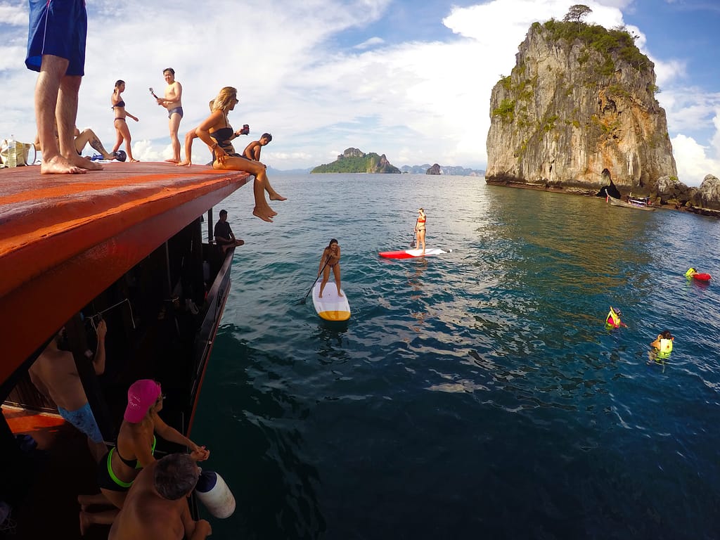 Guests on Krabi Sunset Cruise boat watching people swimming and paddleboarding in the sea with islands in the background in Krabi