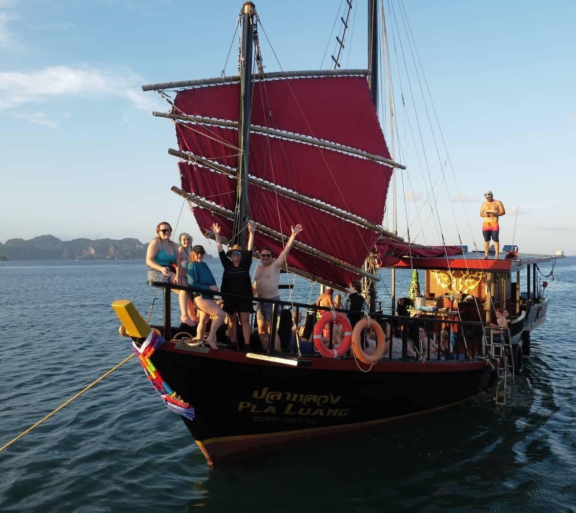 Guests aboard the Krabi Sunset Cruises traditional wooden junk boat with red sails in Krabi, Thailand
