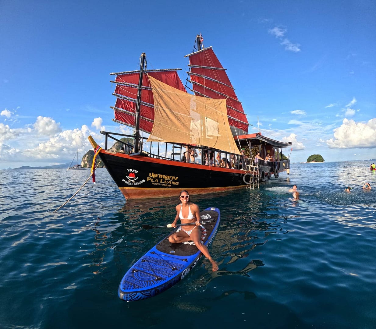 Mujer sentada en una tabla de paddle surf en Krabi, con el barco de la empresa Krabi Sunset Cruises detrás de ella