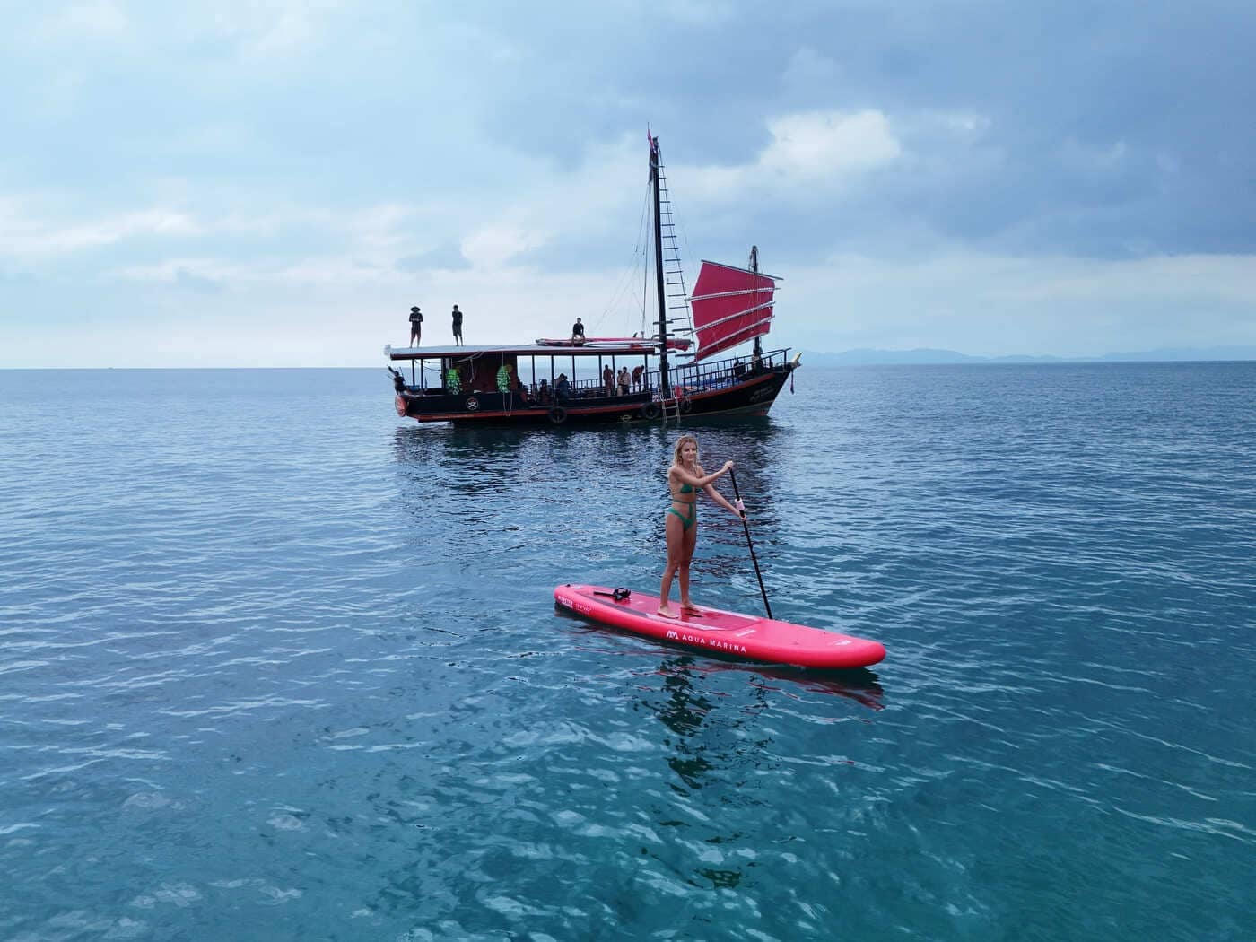 Un visitante practica paddle surf en aguas tranquilas durante una excursión por cuatro islas en Krabi, con un junco al fondo