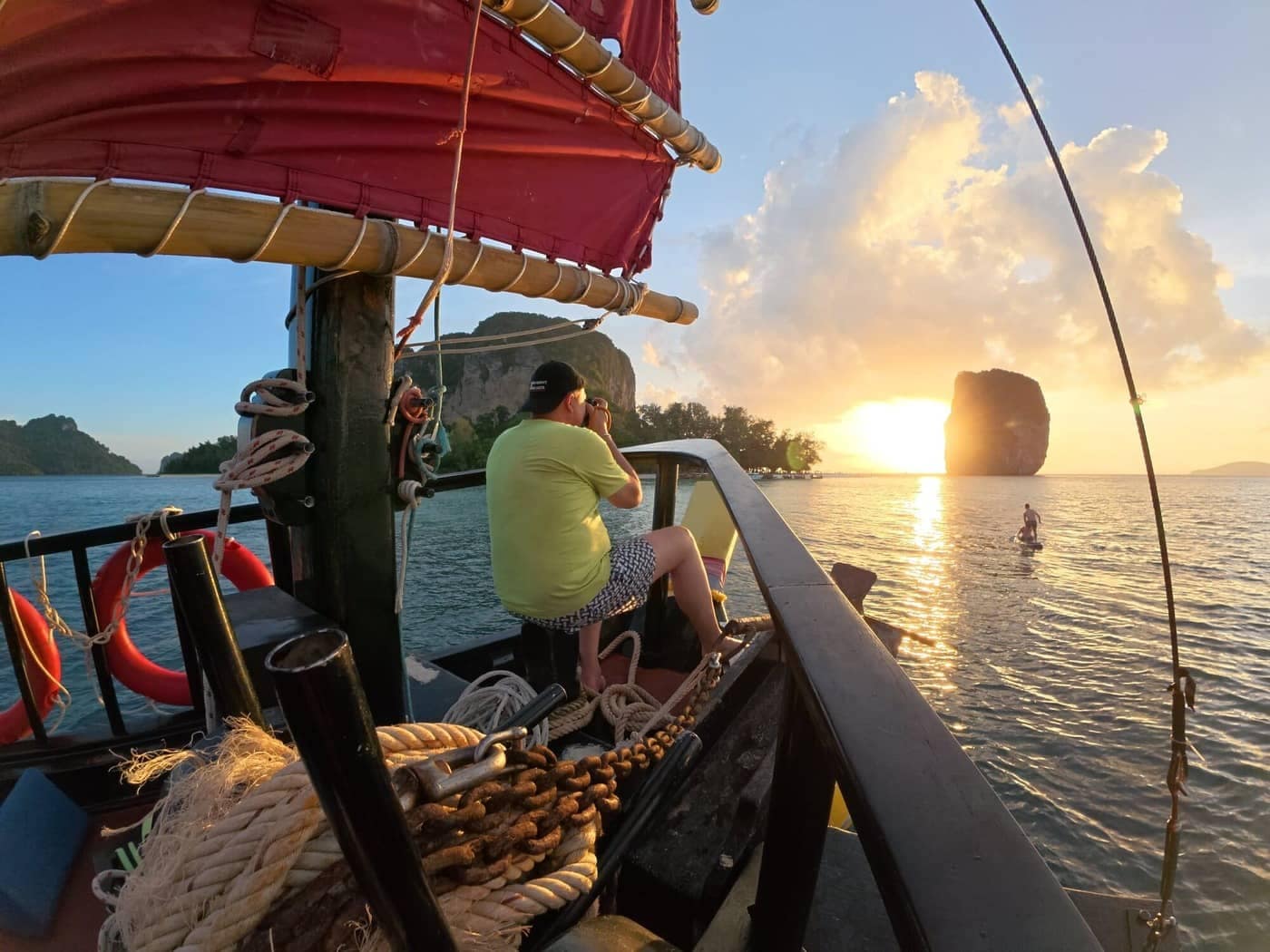 Un turista fotografía la puesta de sol mientras otro practica surf de remo cerca de la isla de Poda, en Krabi