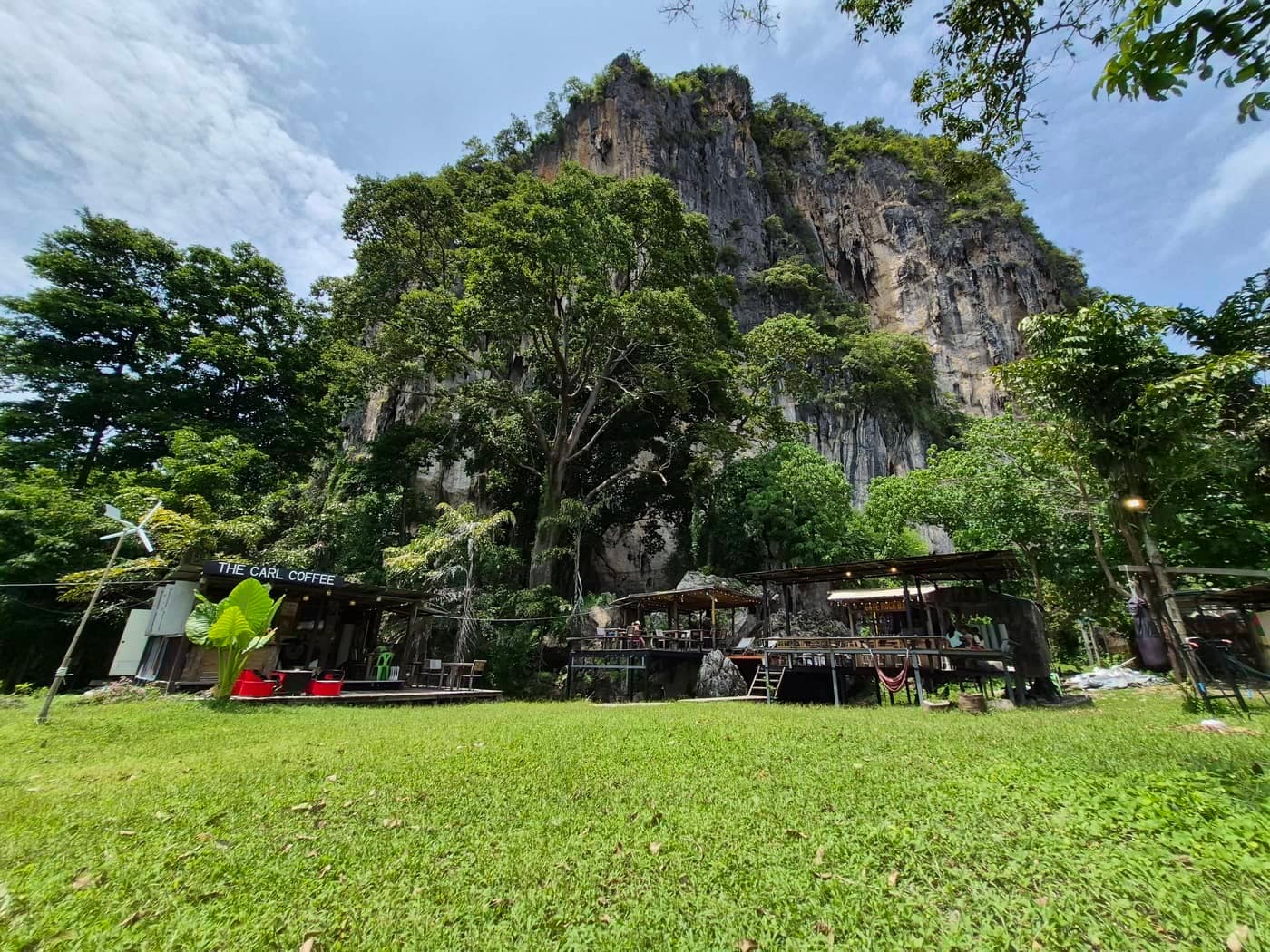 El Cave Rock Bar y la zona de asientos al aire libre se encuentran bajo los imponentes acantilados de piedra caliza de Railay Beach, en Krabi, rodeados de árboles tropicales y un césped.