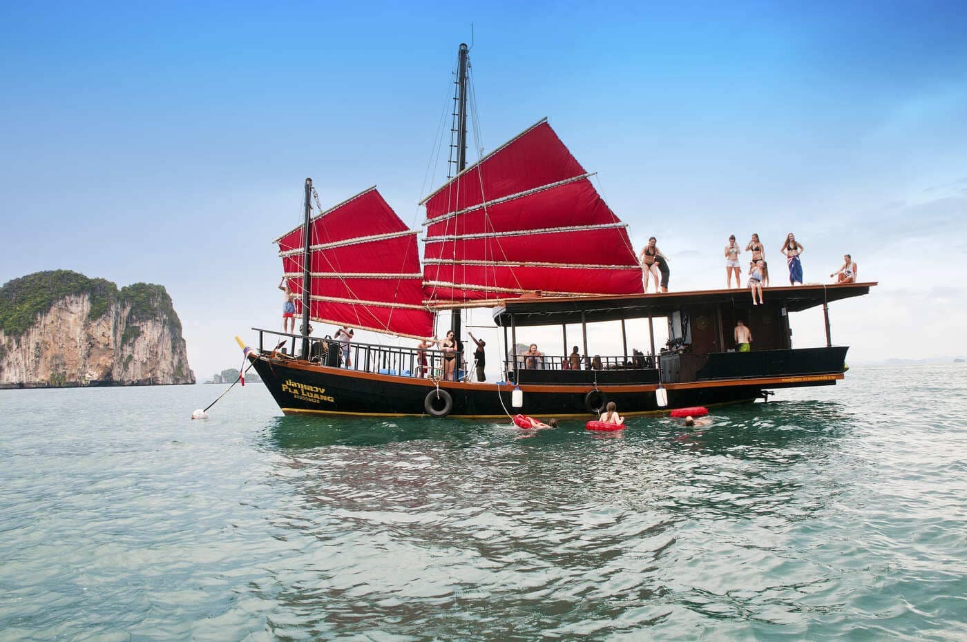Cruceros al atardecer en Krabi: un junco siamés tradicional con velas rojas y huéspedes nadando en Krabi