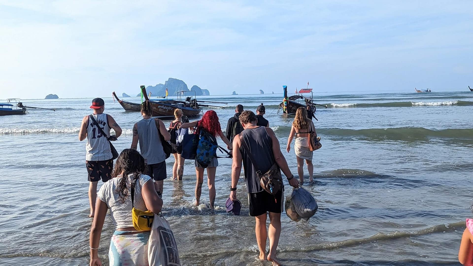 group of people wading into the water to a longtail boat in krabi