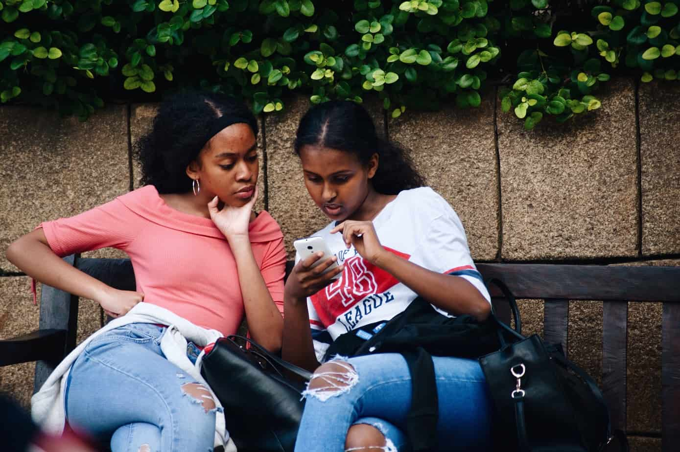 two girls on a bench looking at a smartphone