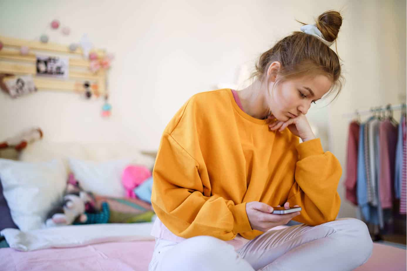 Sexting-Teen-Girl-Holding-Phone-Sitting-in-Bedroom