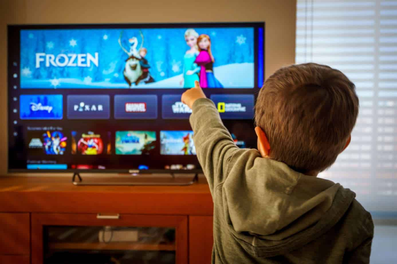 Disney Plus parental control - boy watching disney plus in a living room on a couch pointing the remote at the TV