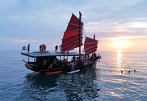 Crucero al atardecer en Krabi: un barco al atardecer con huéspedes practicando paddle surf junto a él y otros disfrutando de la puesta de sol desde la azotea
