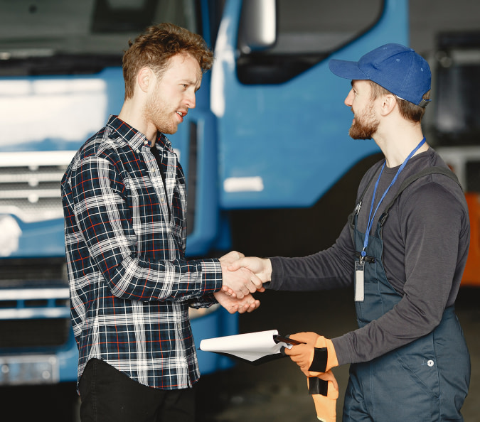 A satisfied customer and a diesel repair specialist shaking hands in front of a truck