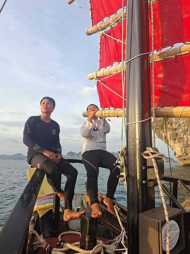 Deux hommes assis à la proue d'une jonque aux voiles rouges