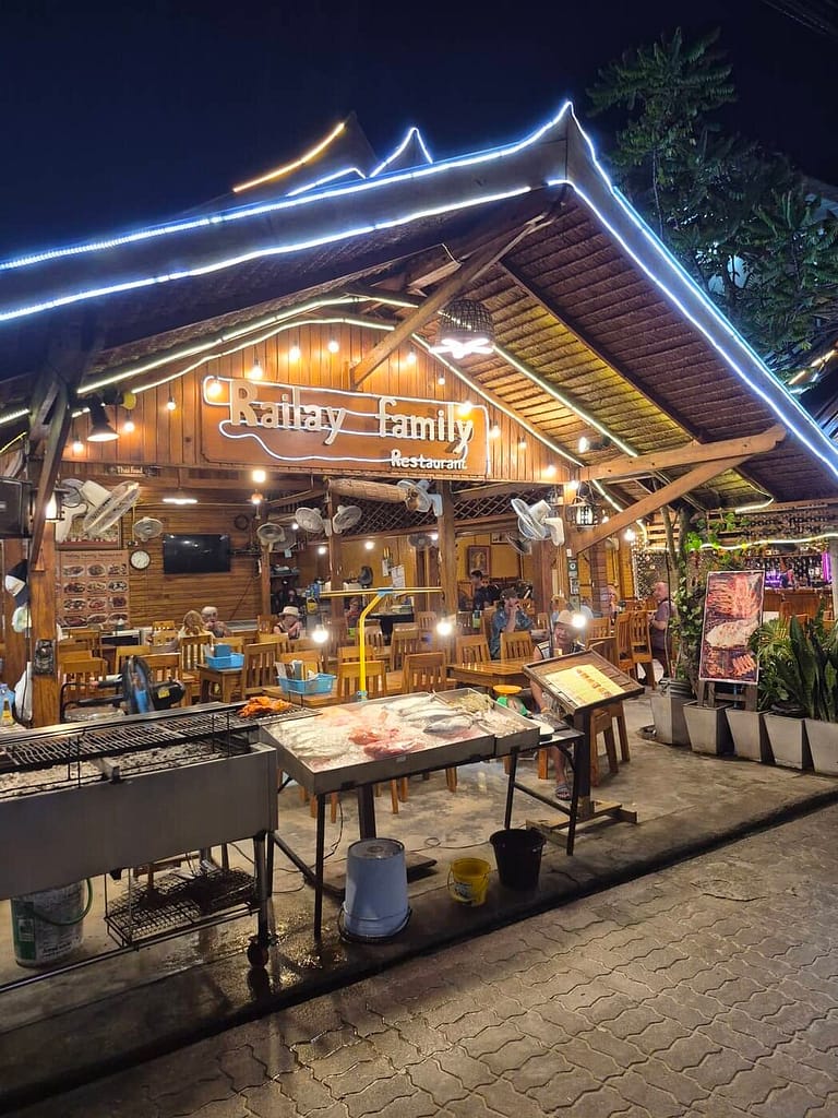 El restaurante Railay Family Restaurant por la noche en la playa de Railay, en Krabi, con mesas de madera al aire libre, señalización iluminada y una exposición de mariscos frescos.