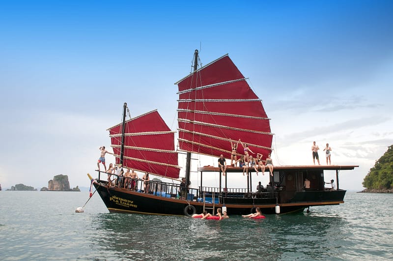 Barco de «Krabi Sunset Cruises» amarrado frente a la Isla del Pollo, con los pasajeros divirtiéndose en la cubierta y en el agua.