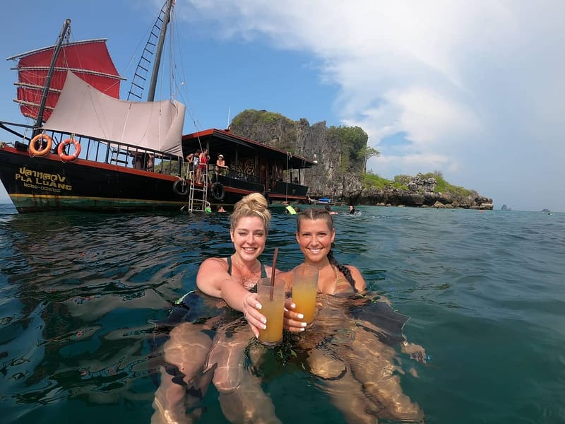 Deux filles en train de boire des cocktails dans l'eau, avec un bateau de type « junk » derrière elles.