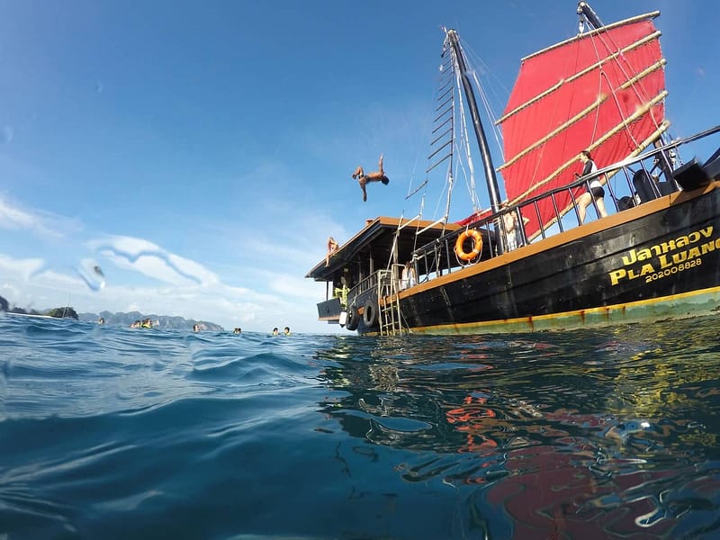 Une personne faisant un doigt d'honneur depuis le toit d'un vieux bateau aux voiles rouges à Krabi
