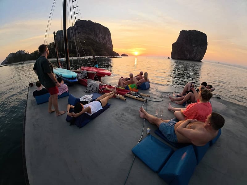 Des visiteurs se détendent sur le pont supérieur d'une jonque tout en admirant le coucher de soleil entre les îles calcaires de Krabi
