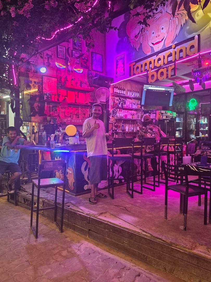 El Tamarind Bar en la calle Railay por la noche, con iluminación colorida en tonos rosa y púrpura, un bar de cócteles al aire libre y clientes que se relajan.