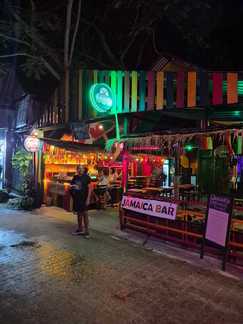 Jamaica Bar en Railay Walking Street por la noche, con decoraciones coloridas en estilo reggae, luces de neón, un bar al aire libre y asientos al aire libre.