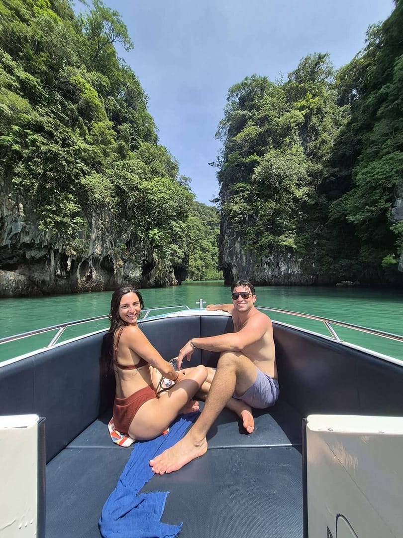 Una pareja sentada en la proa de una lancha motora en Krabi, con acantilados de piedra caliza a sus espaldas.