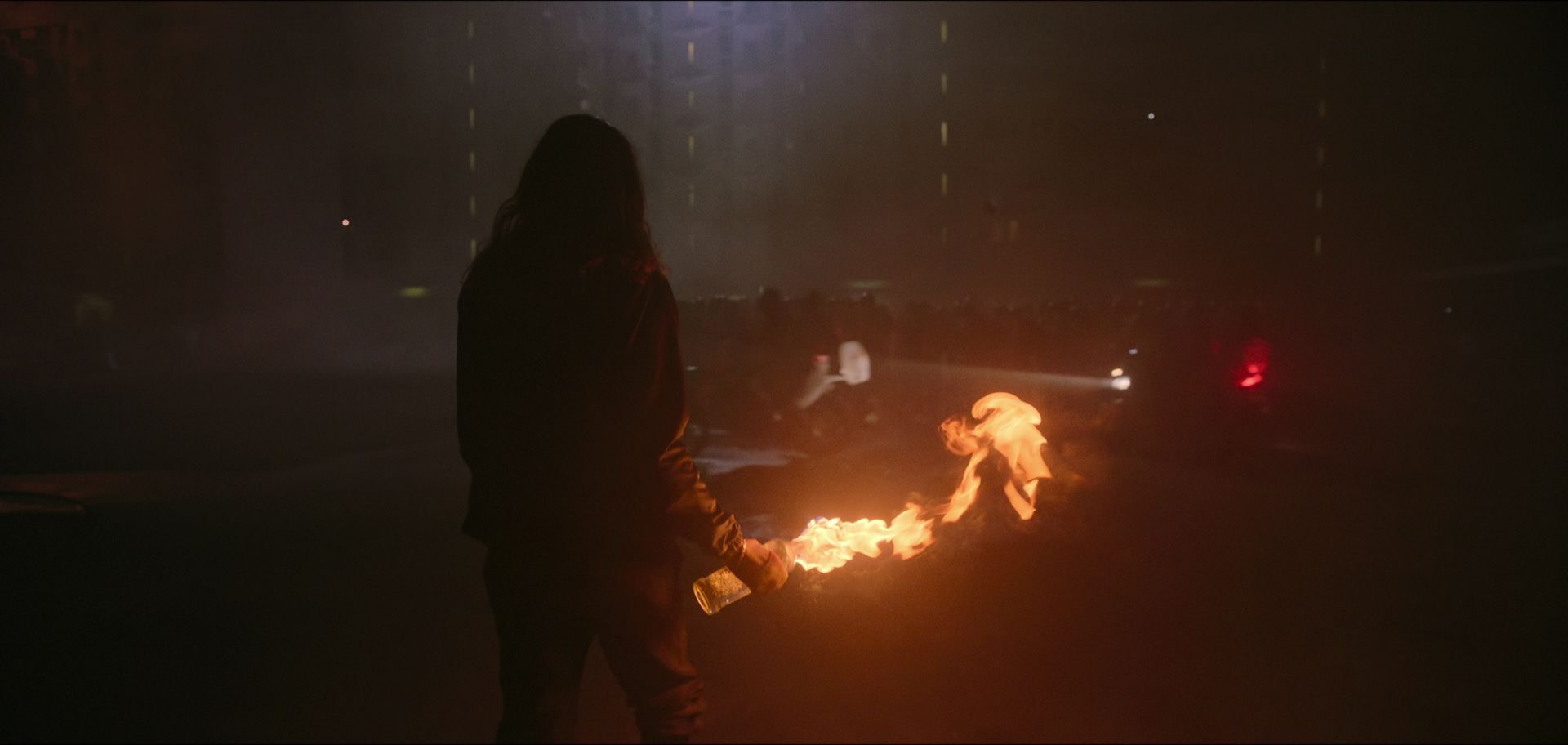 A silhouetted figure holding a flaming Molotov cocktail stands on the streets of Paris in Athena