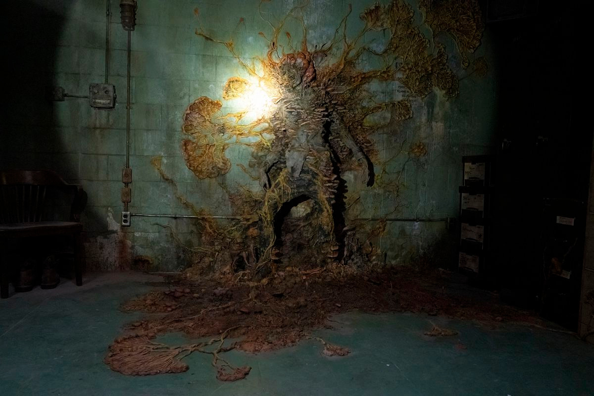 A shot of an infected person stuck to a wall with overgrown mushrooms in The Last of Us