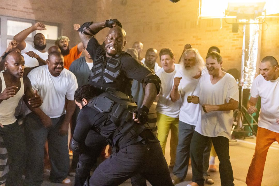 A man in body armor (Tyrese Gibson) struggles his way out of being tackled by another man in body armor as a crowd of men scream and cheer around them.