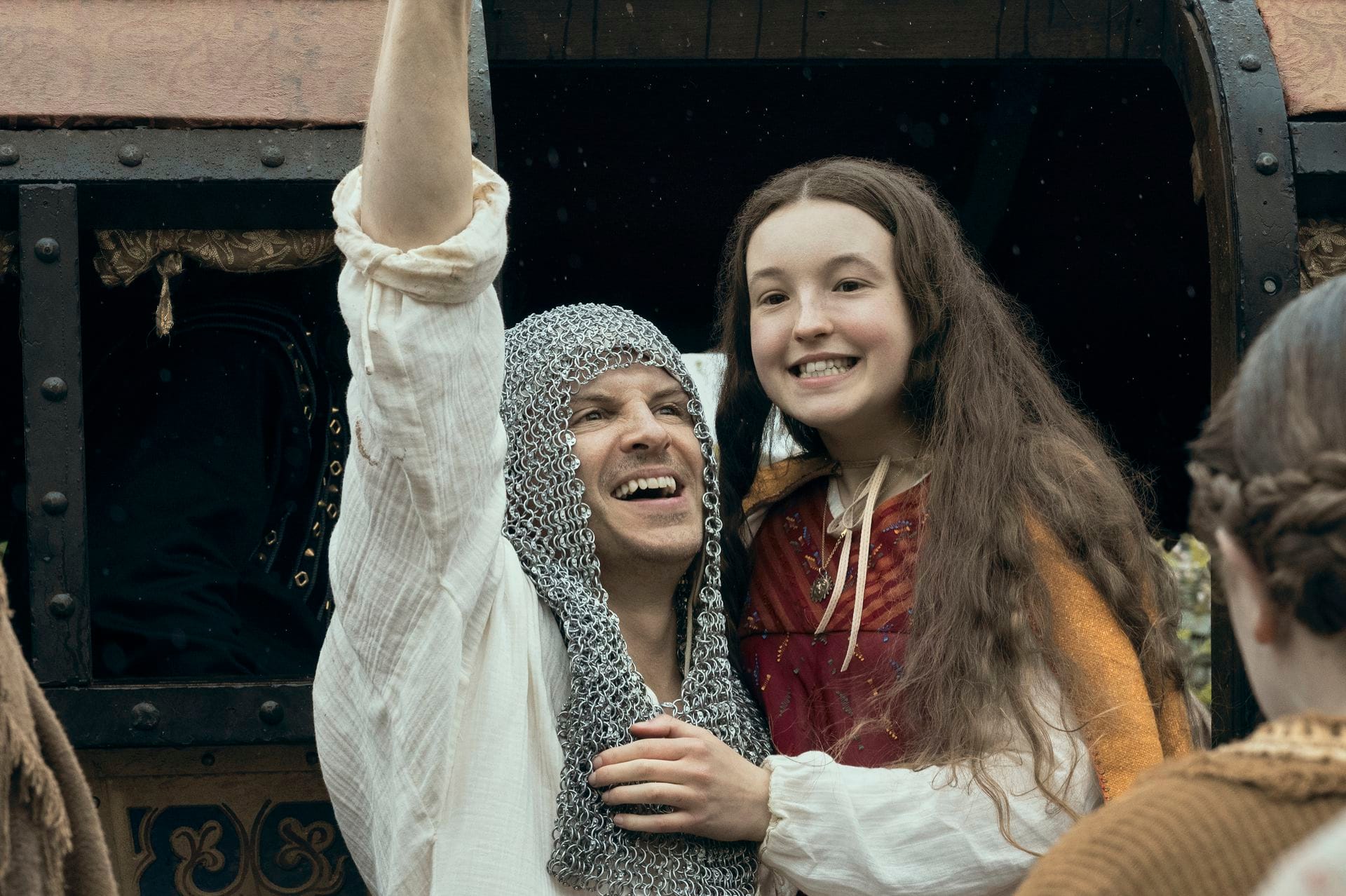 a man wearing a chainmail snood holds up a young teenage girl 