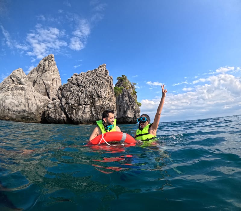 Two snorkelers in life jackets floating near rocky limestone cliffs in clear waters off Krabi